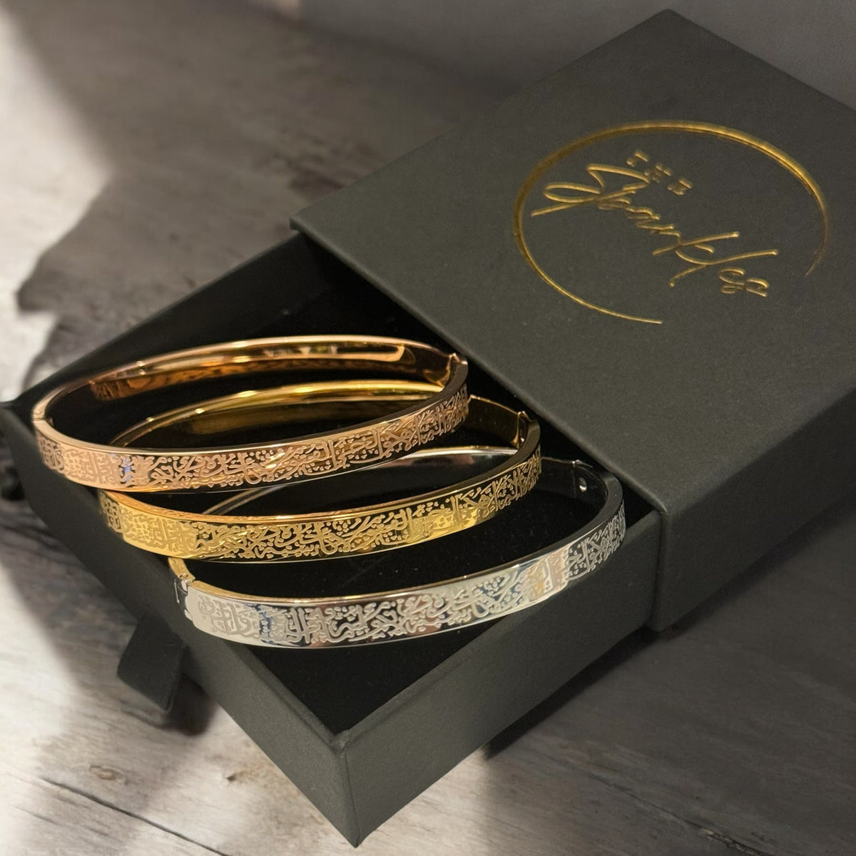 Set of gold bangles in a black box with a brand logo on a wooden surface