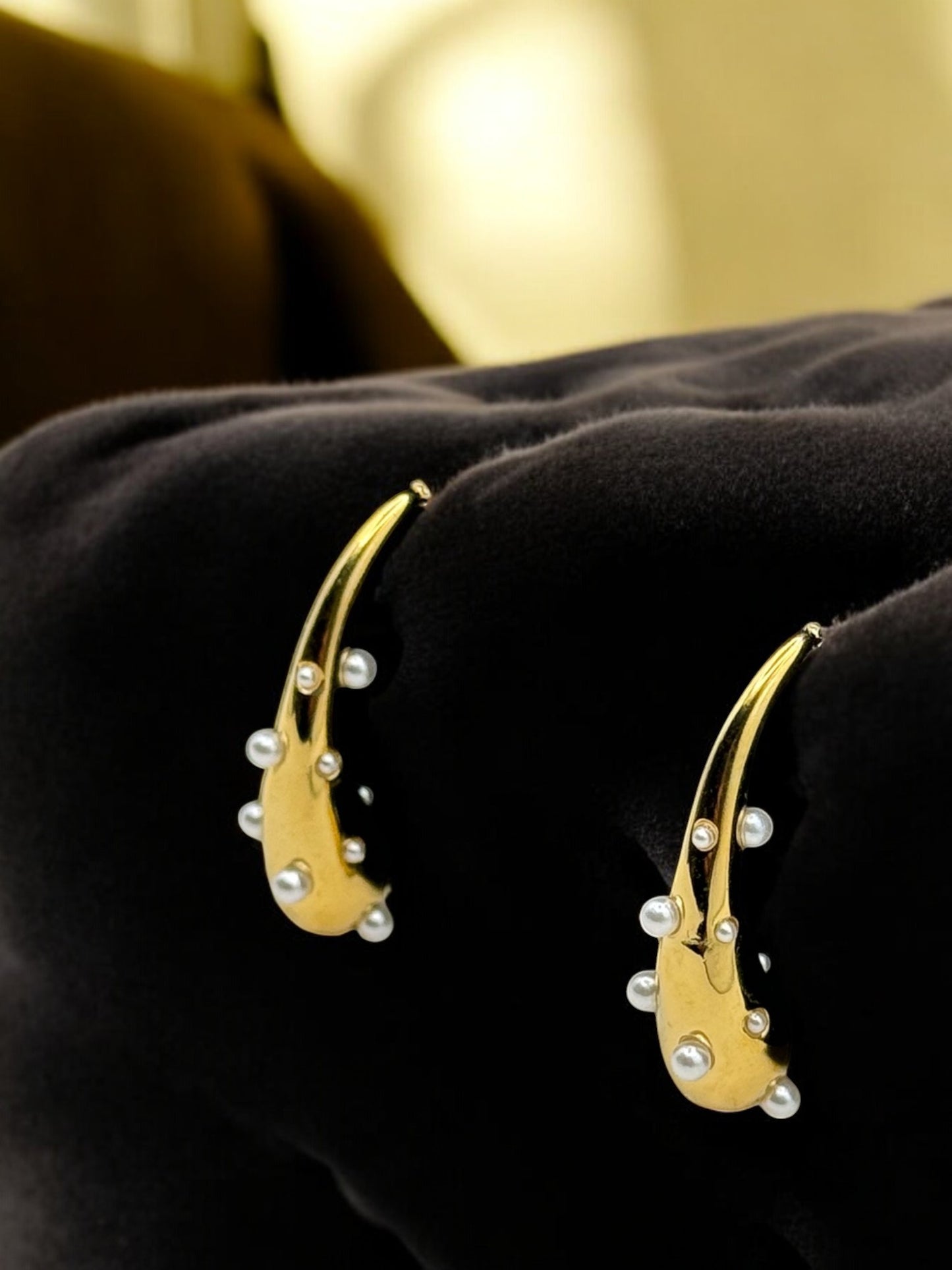 A close-up image of a pair of pearl drop earrings with a golden metal band and small pearl accents on the top part of the earrings.