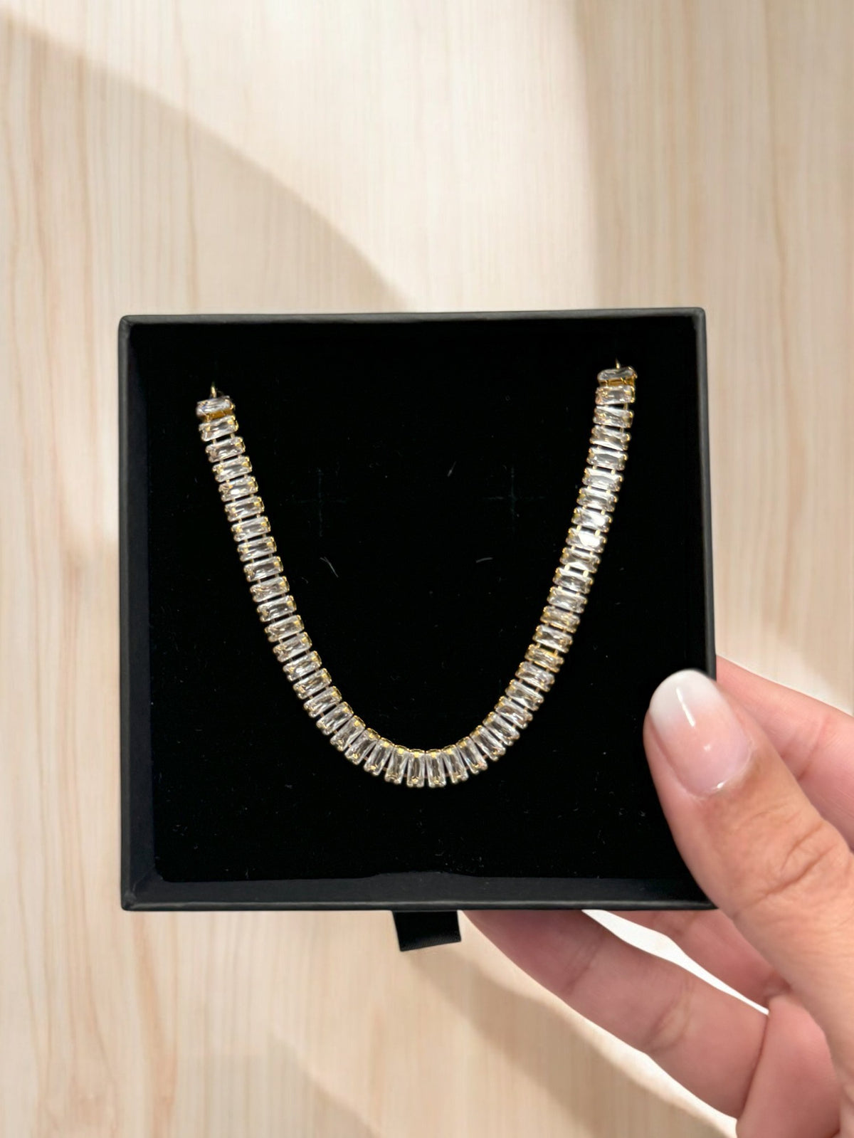 A gold-plated bracelet adorned with zircon stones, presented in a black drawstring pouch.