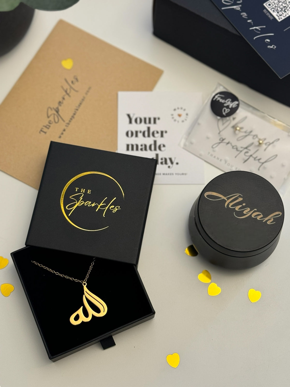 A customized gift box with jewelry and a scented candle. The jewelry is displayed in a black box with a gold necklace, and the candle has an engraved lid with the name 'Ally'.
