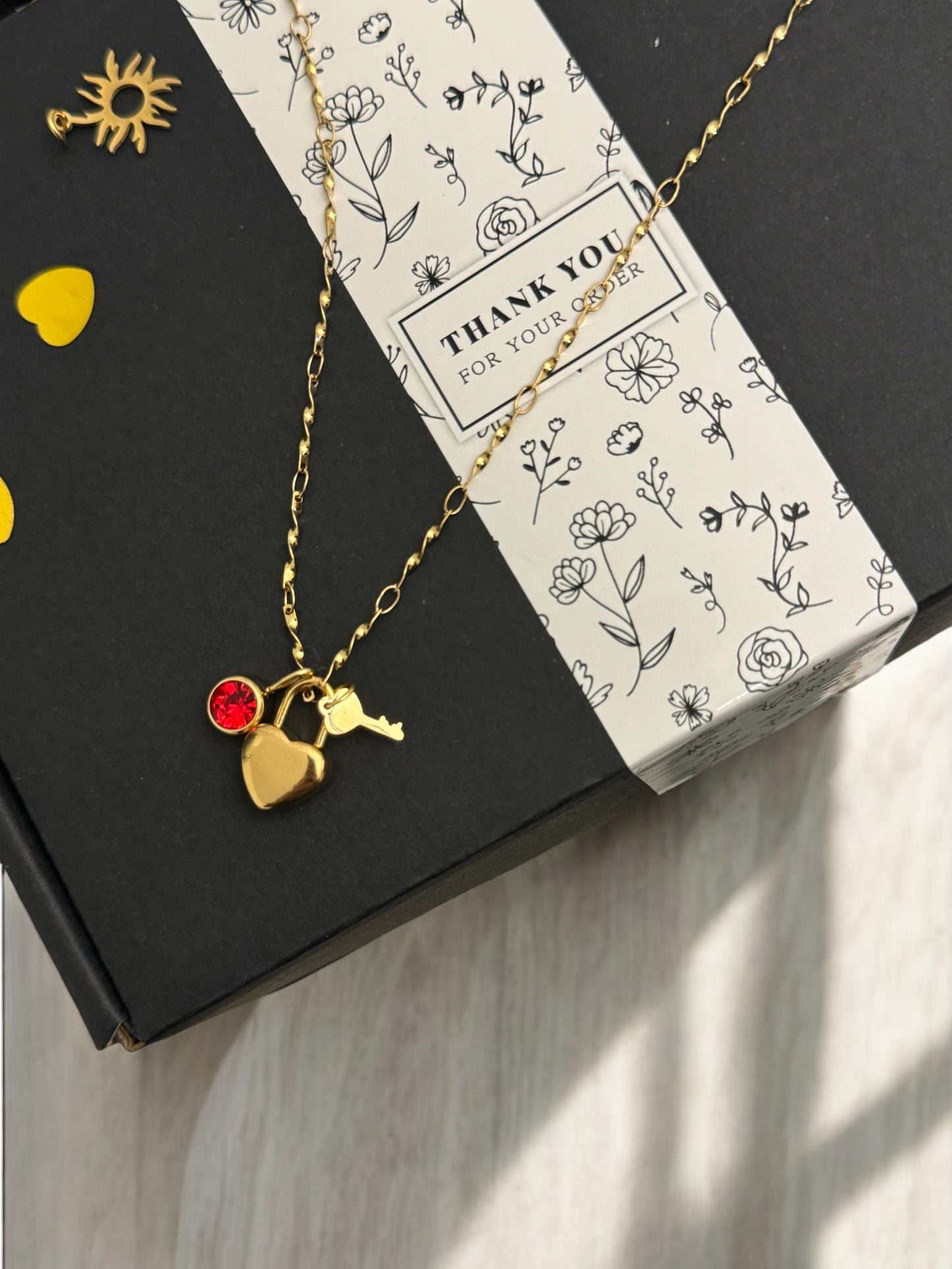 A gold-plated charm necklace with multiple charms, presented on a box with a 'Thank you' note.