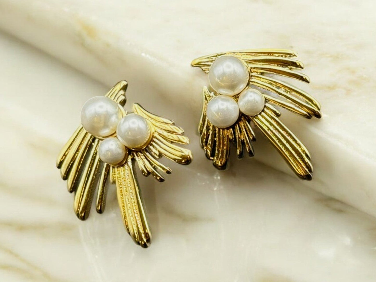 A pair of gold-colored earrings with pearl drops on a marble surface.