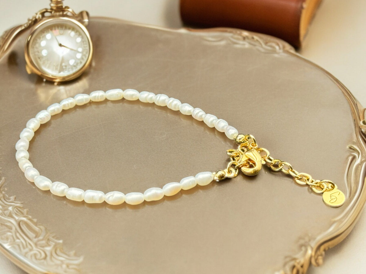 A bracelet featuring a series of freshwater pearls strung on a gold-colored chain, displayed on a silver bracelet holder.