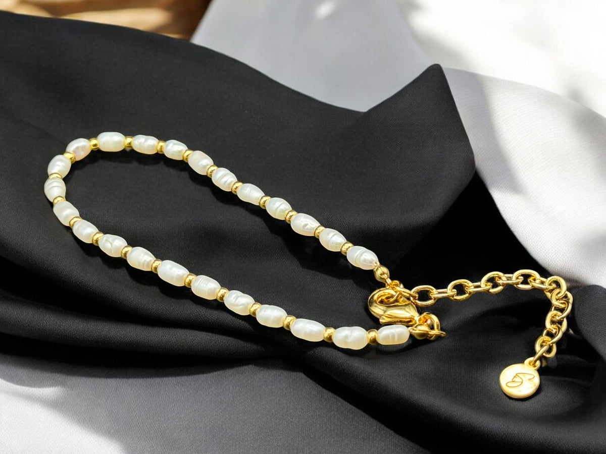 A luxurious bracelet featuring freshwater pearls and gold beads, displayed on a black silky fabric.