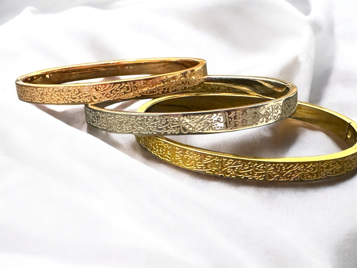 Three gold bangles with intricate designs on a white background