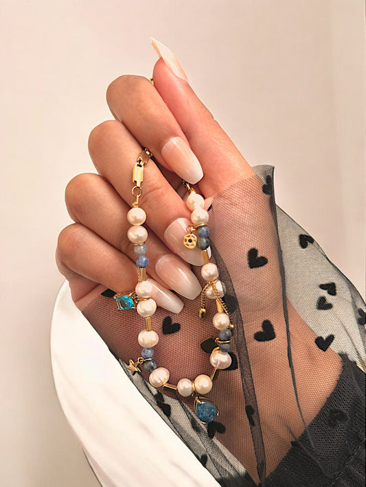 A close-up image of a woman's hand showcasing a formal necklace with pearls and gemstones, including a heart-shaped charm.