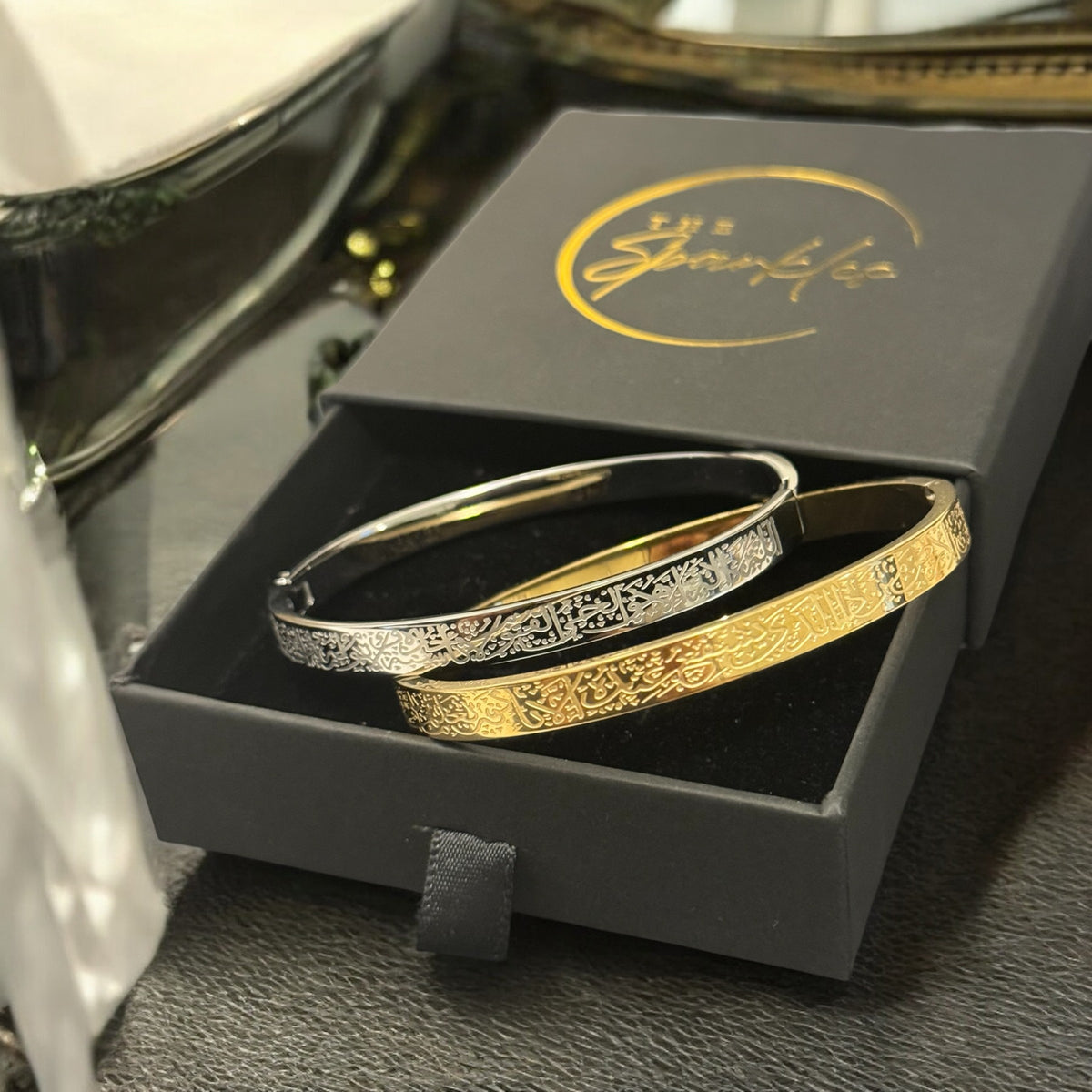 Two gold and silver bracelets in a branded box on a dark surface.